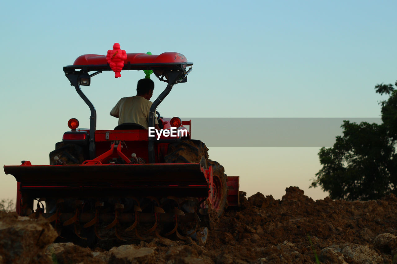 Rear view of man in tractor ploughing field against sky