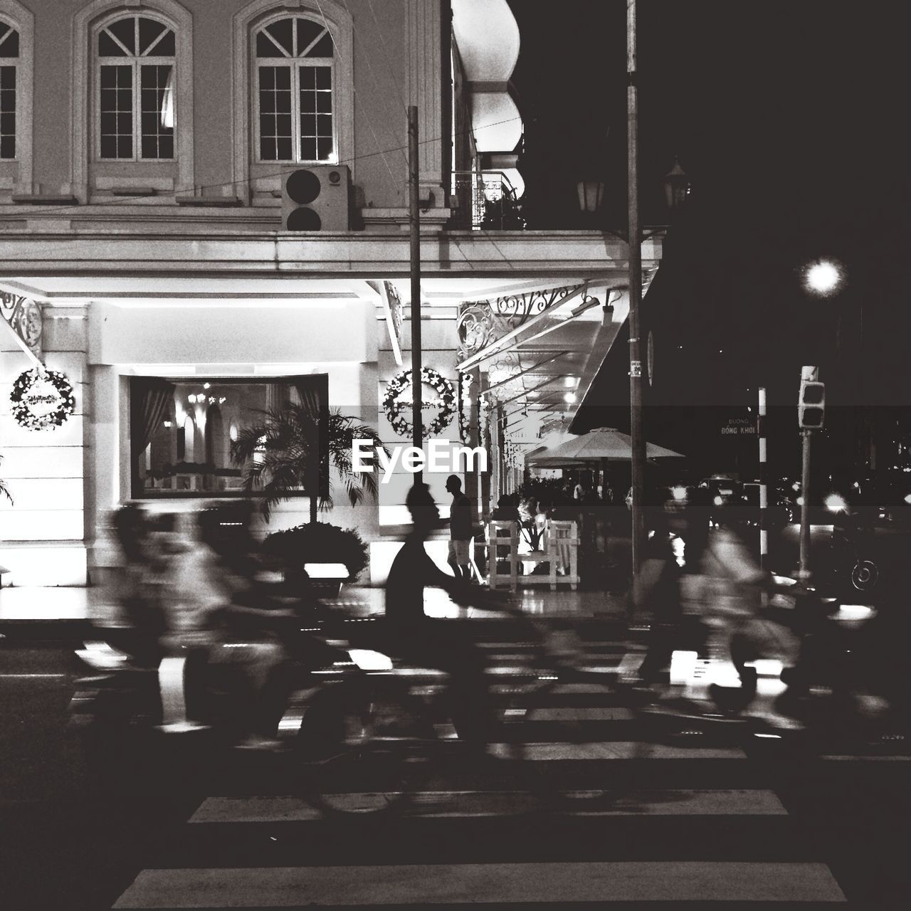 People riding motorcycle on street by sidewalk cafe