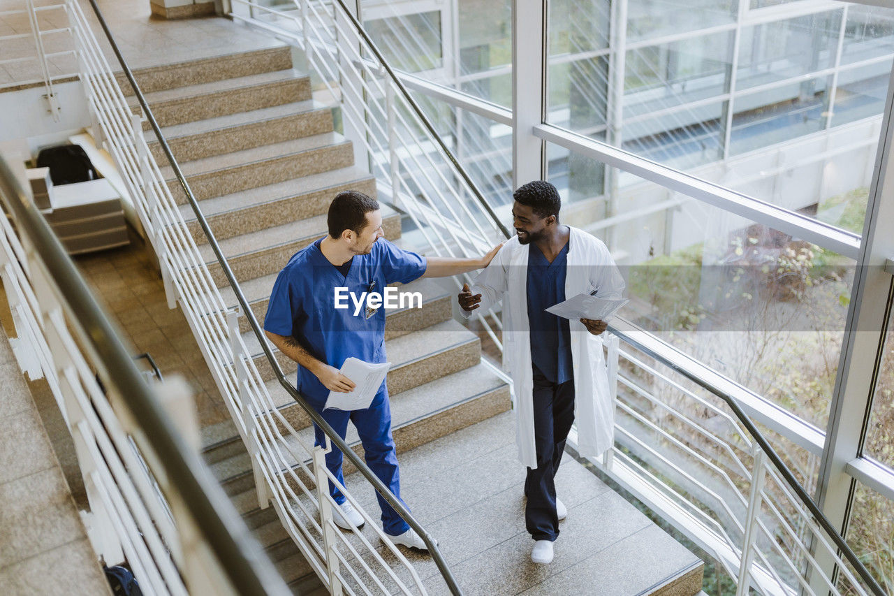 High angle view of smiling male doctor and nurse discussing while moving down on staircase in hospital
