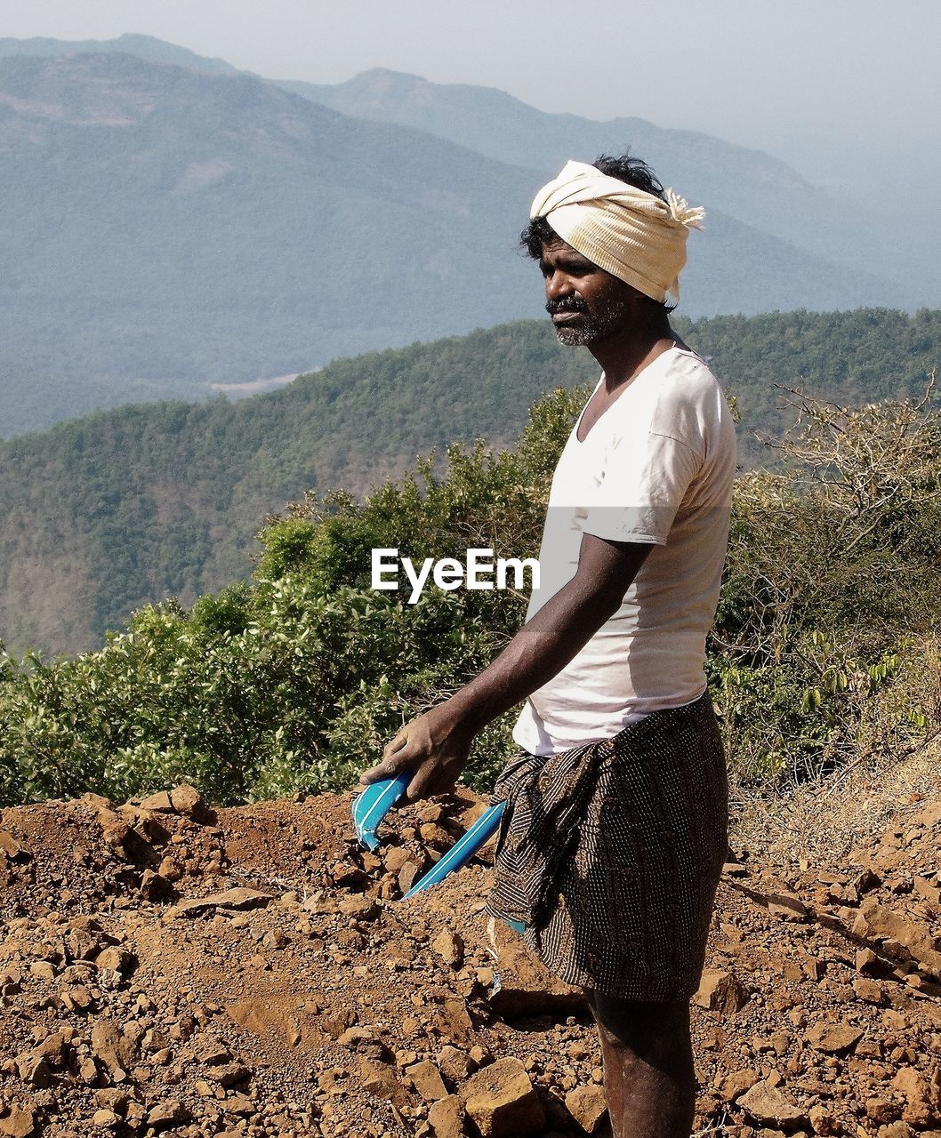 MAN STANDING BY PLANTS AGAINST MOUNTAINS