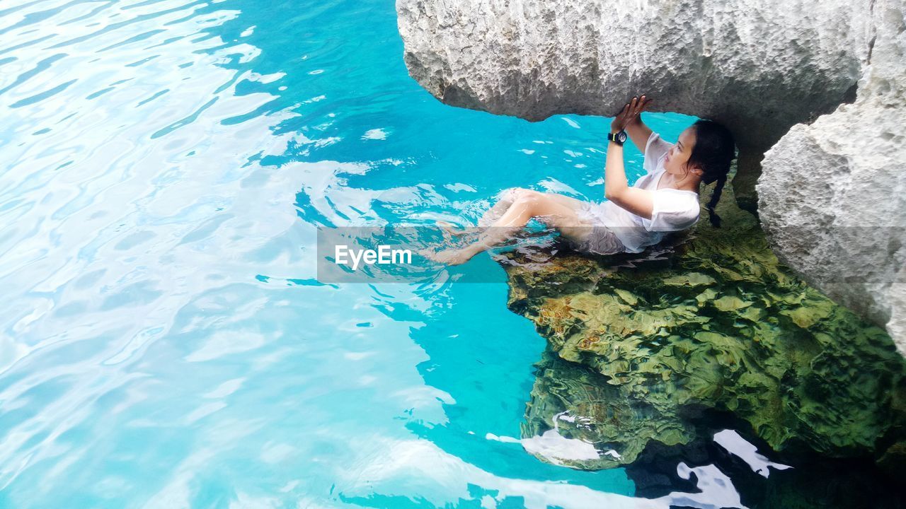 Full length of woman relaxing on rock in sea