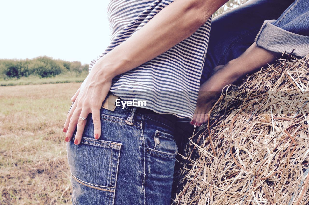 Midsection of couple embracing by hay at field