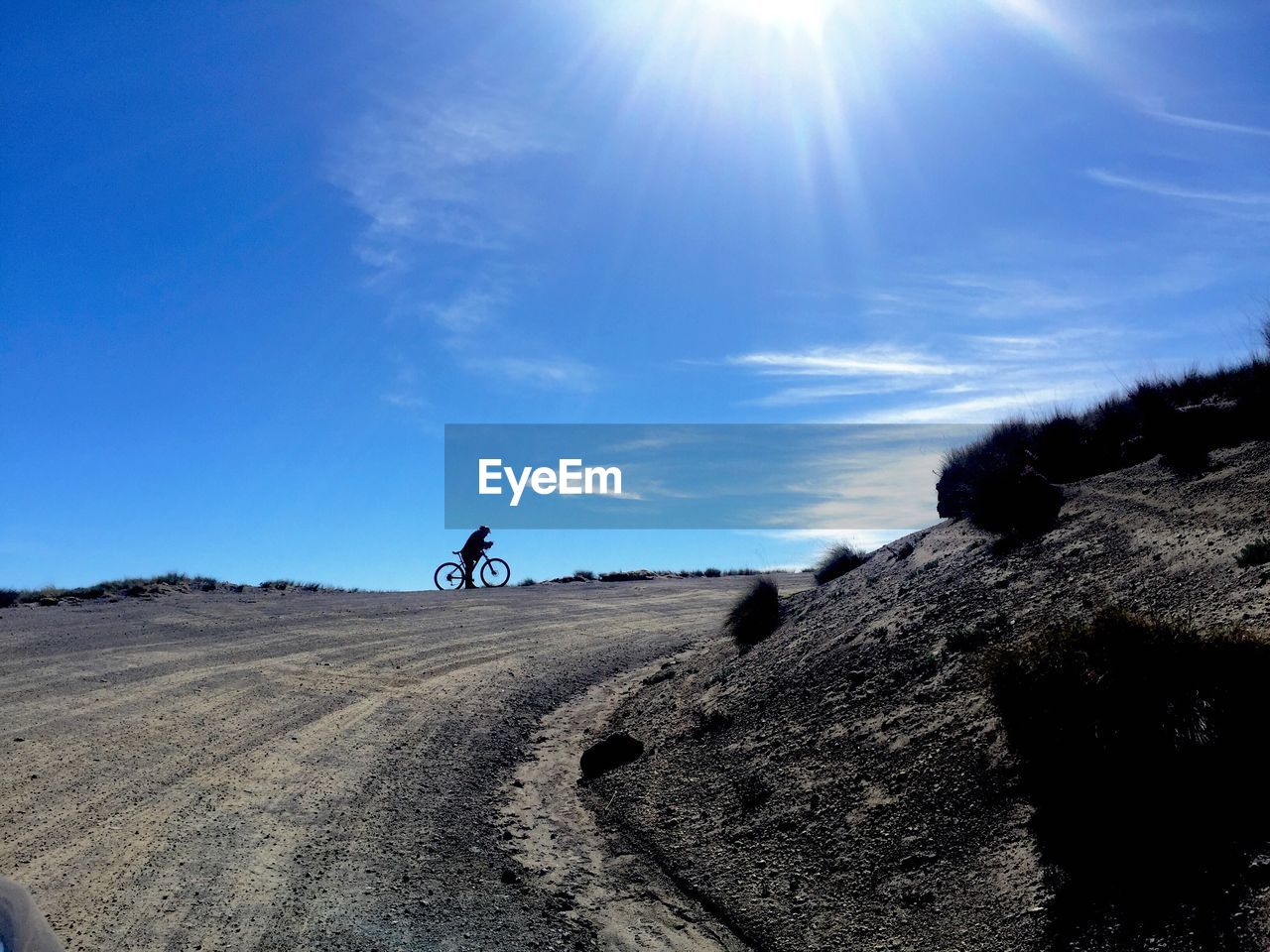 Man riding bicycle on dirt road against blue sky