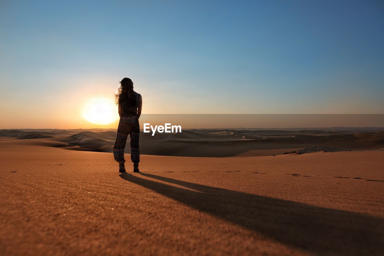 Silhouette woman walking on beach against clear sky during sunset