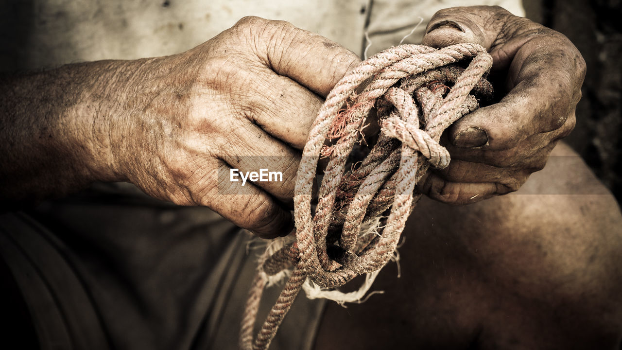 Midsection of old man tying rope