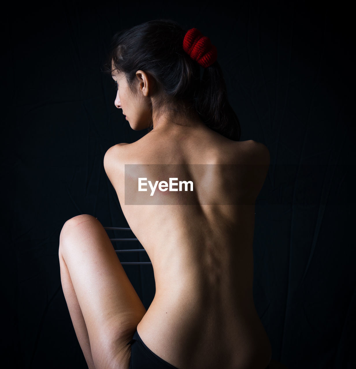 Rear view of shirtless young woman against black background