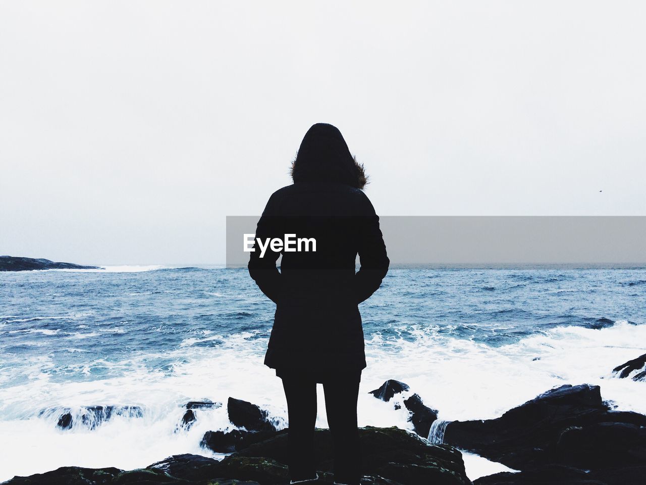 Rear view of woman standing on rock at shore against sky