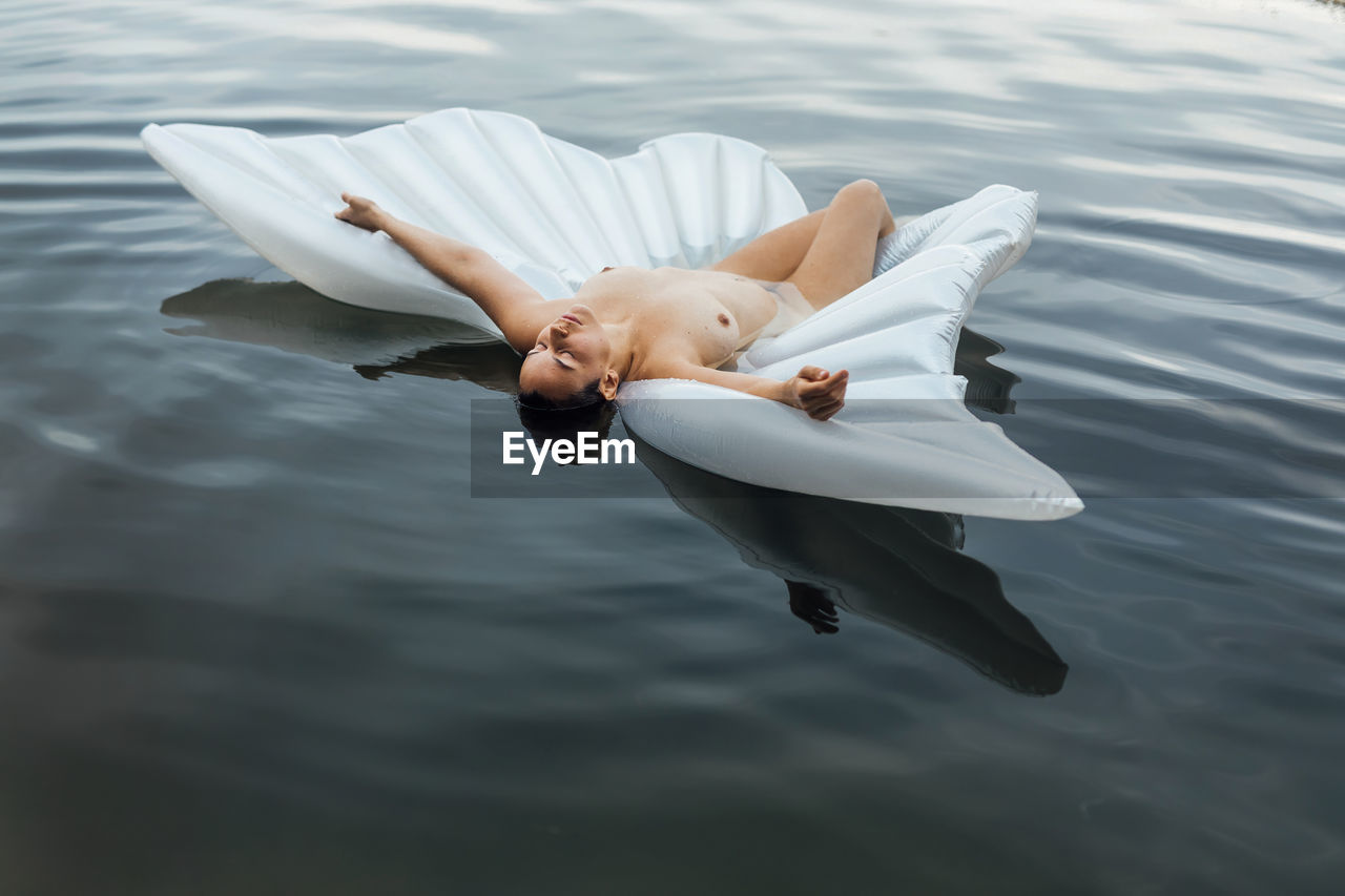 High angle view of sensuous woman lying over inflatable raft in lake