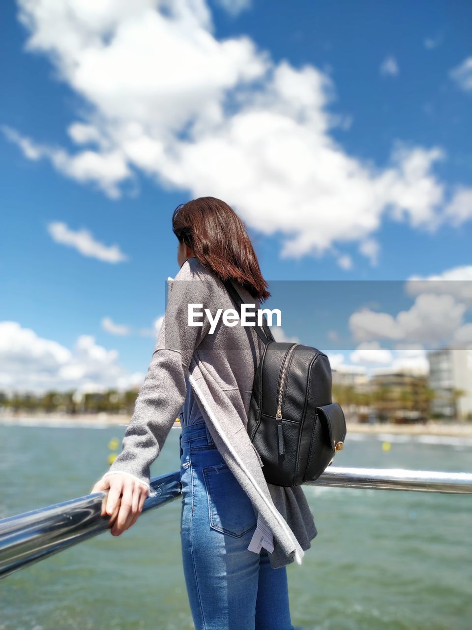 REAR VIEW OF WOMAN STANDING AGAINST RAILING