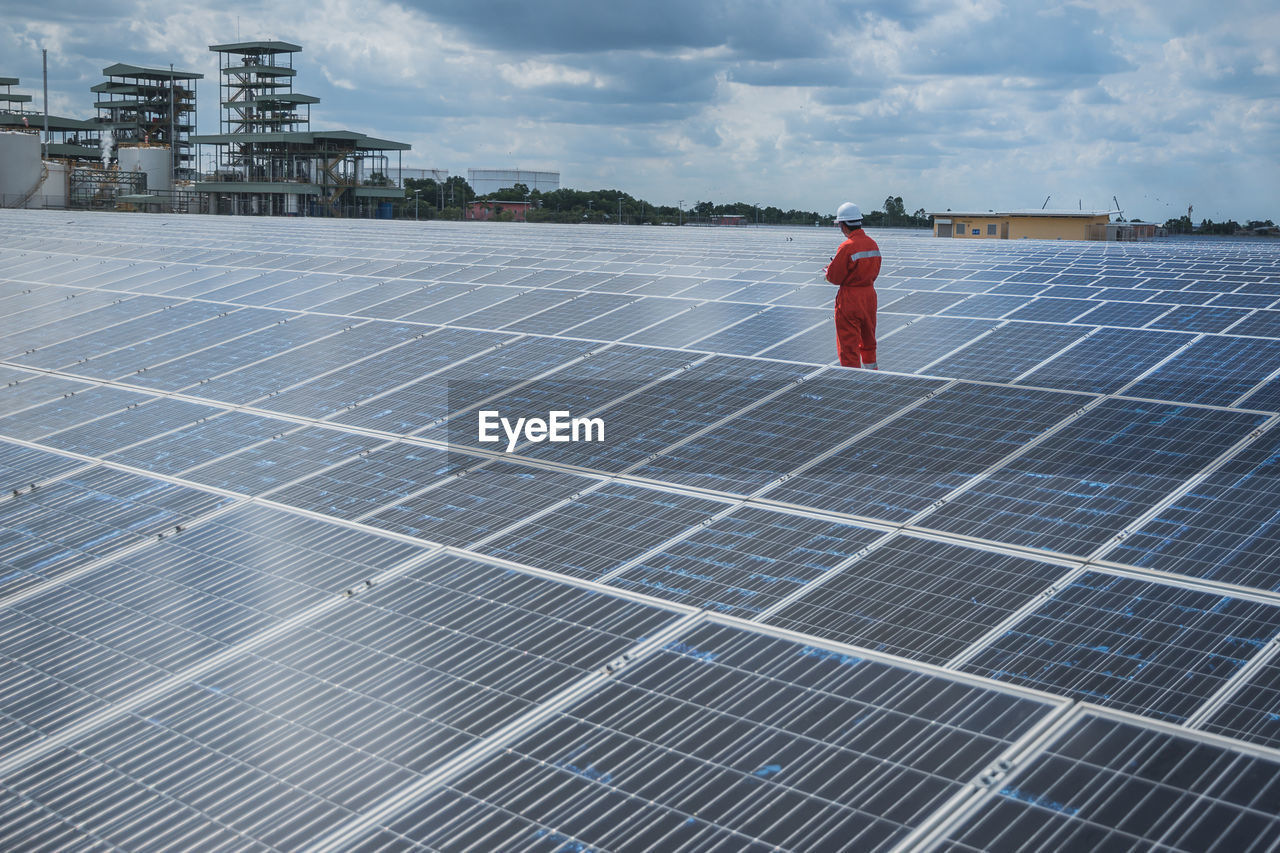 Manual worker working amidst solar panels against sky