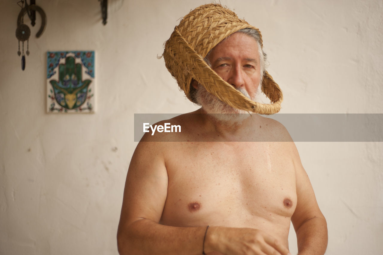 Shirtless senior man wearing wicker basket at home