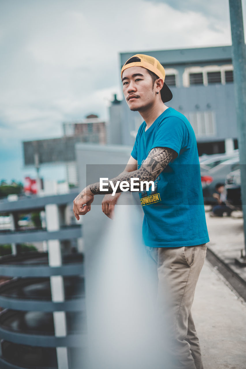 Thoughtful young man looking away while standing by railing in city