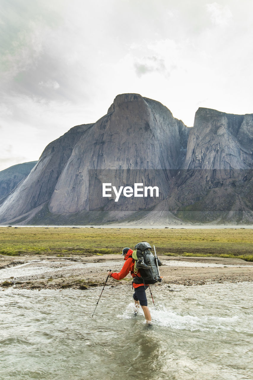 Backpacker crosses river below mountains in akshayak pass