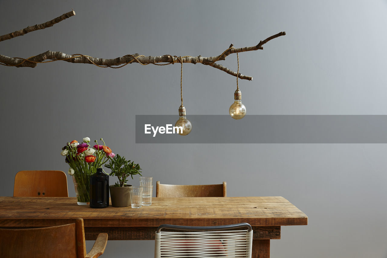 Light bulb hanging on wood over dining table against wall