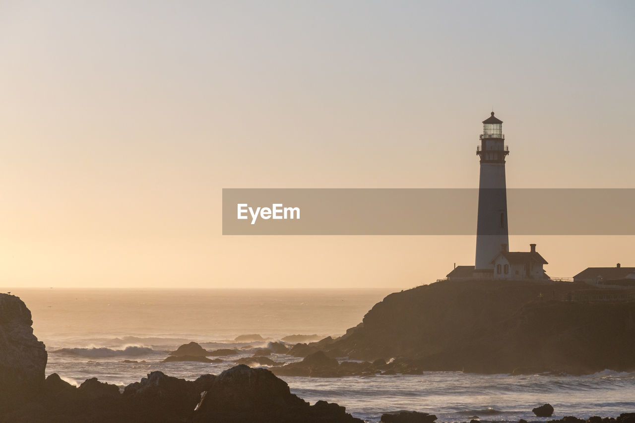 Lighthouse by sea against sky during sunset