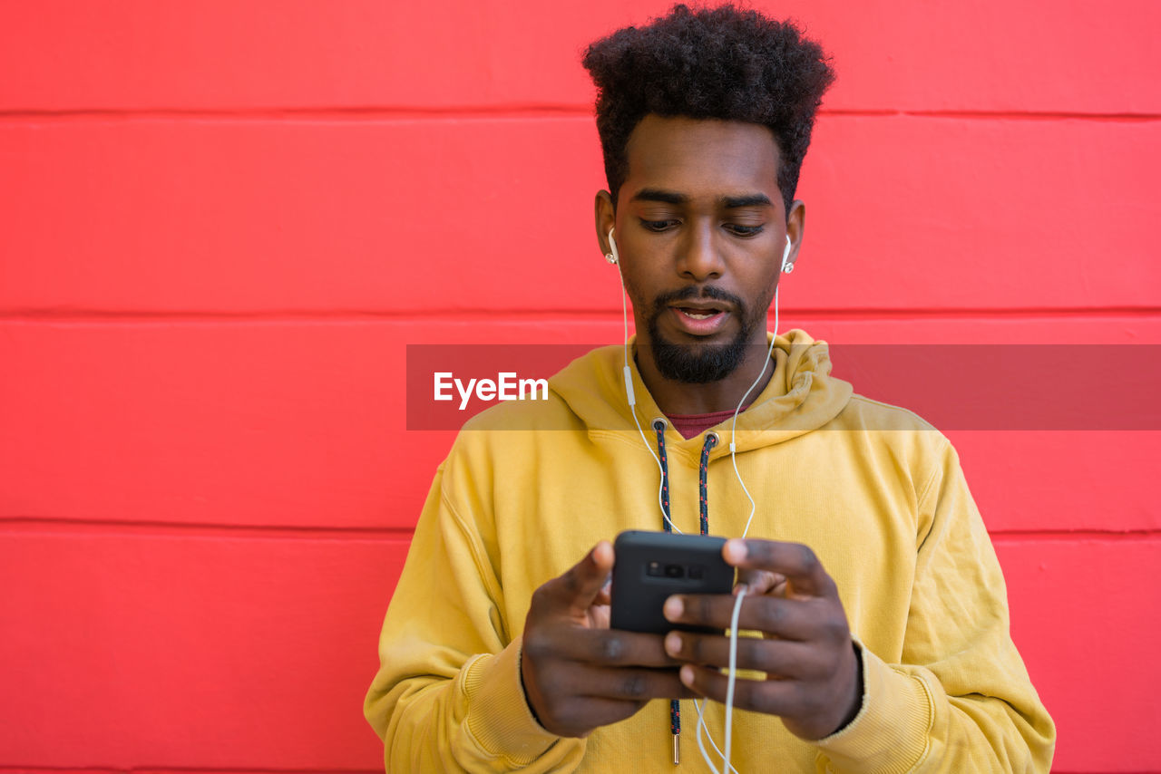 PORTRAIT OF SMILING MAN HOLDING CAMERA WHILE STANDING AGAINST RED WALL