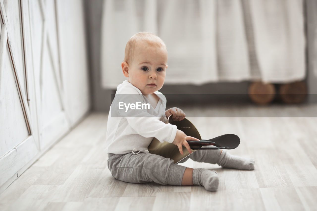 Baby son playing on the floor with kitchen utensils in a real bright interior, lifestyle style.
