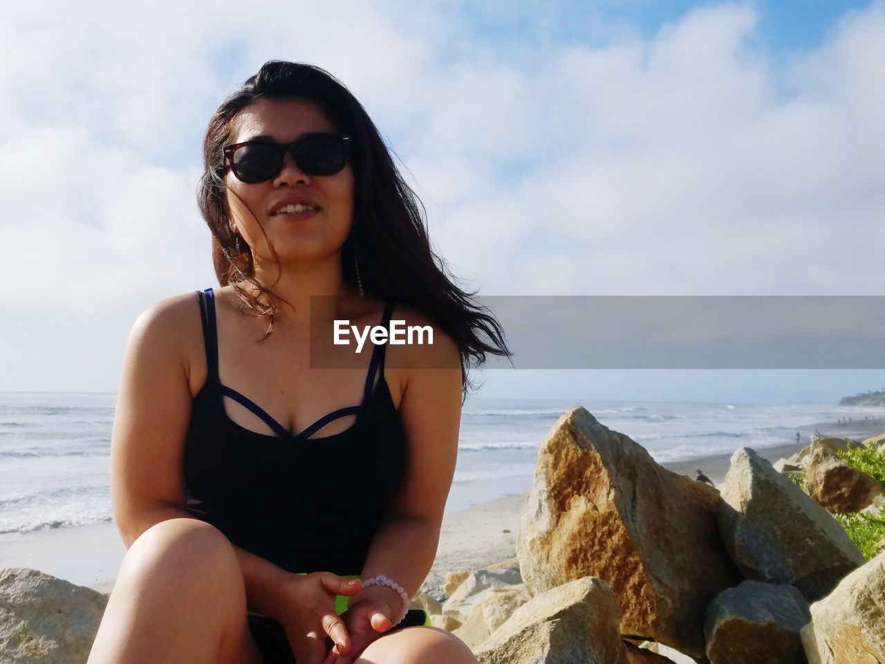 Smiling woman wearing sunglasses while sitting at beach against sky