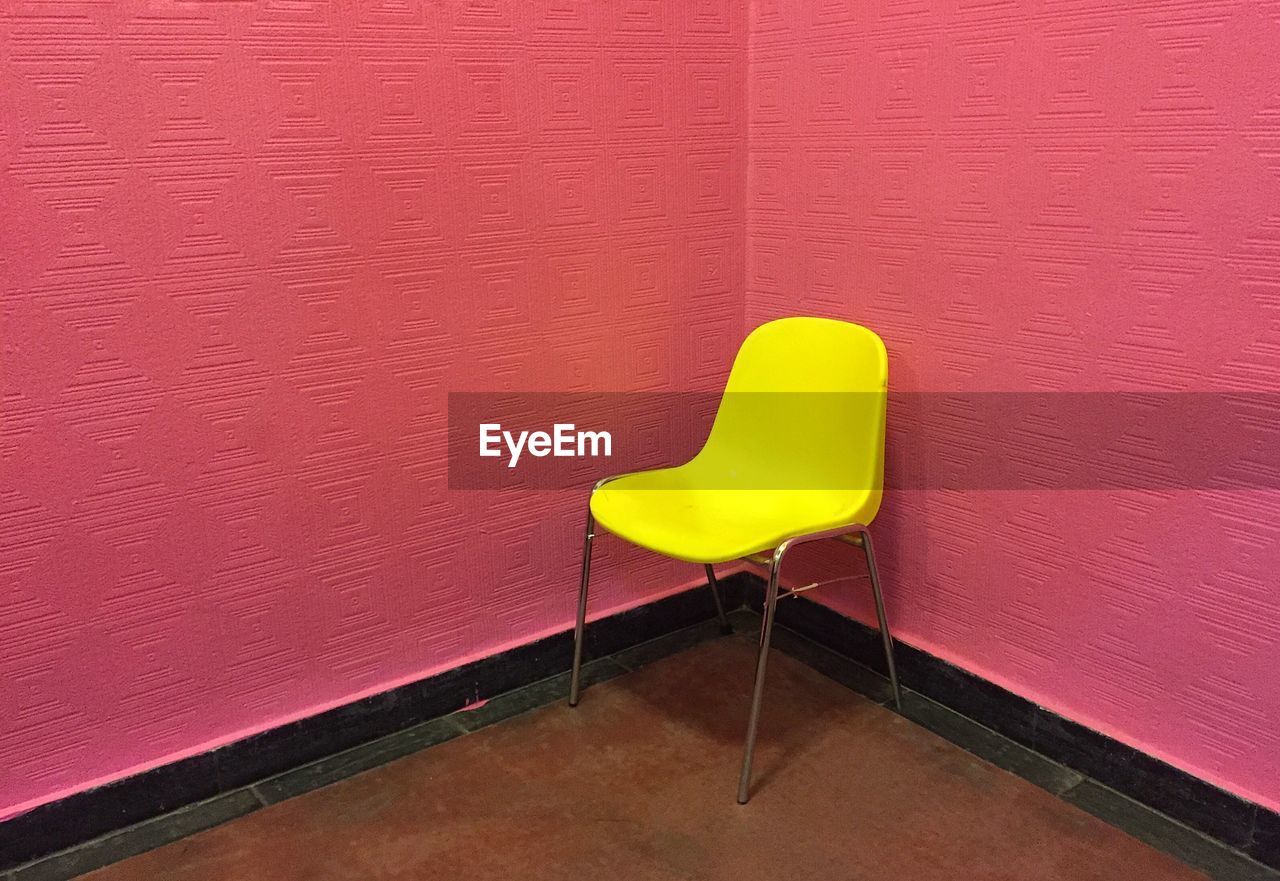 High angle view of empty yellow chair against pink wall in room