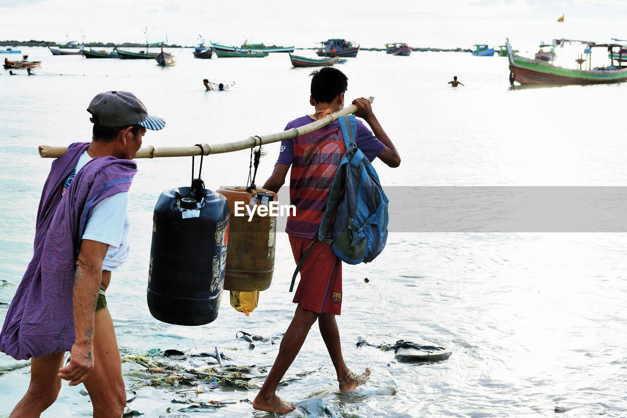 REAR VIEW OF MEN STANDING ON BOAT AT BEACH