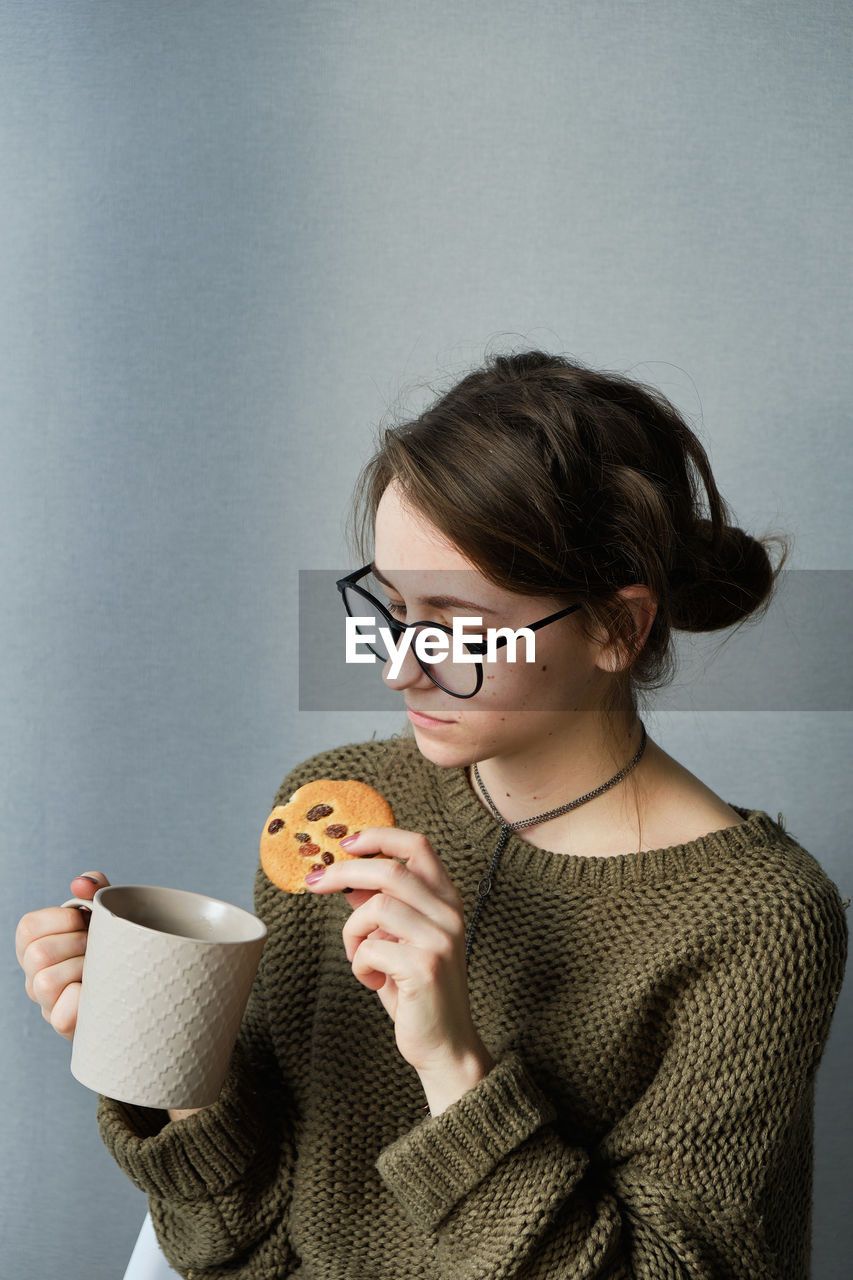 Millennial brown-haired girl in glasses drinking tea with cakes alone