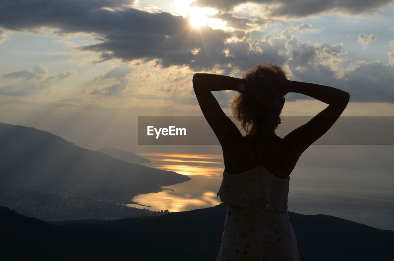 Woman with arms raised standing on mountain against sky during sunset