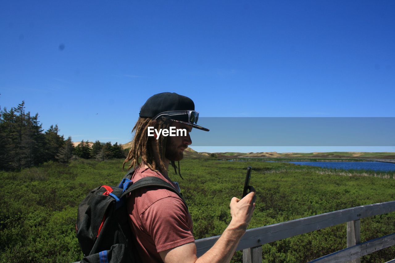 Side view of young man photographing on pier through smart phone