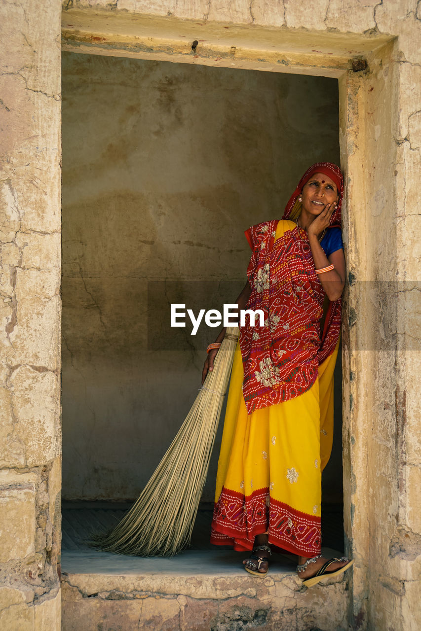 Portrait of woman with broom standing at door of house