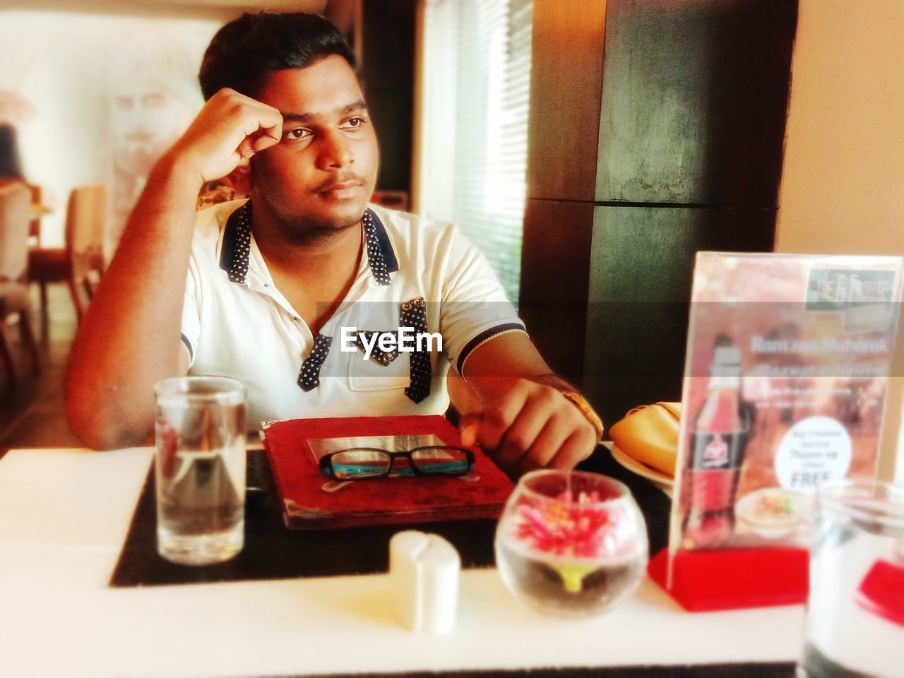 PORTRAIT OF YOUNG MAN SITTING ON TABLE AT RESTAURANT