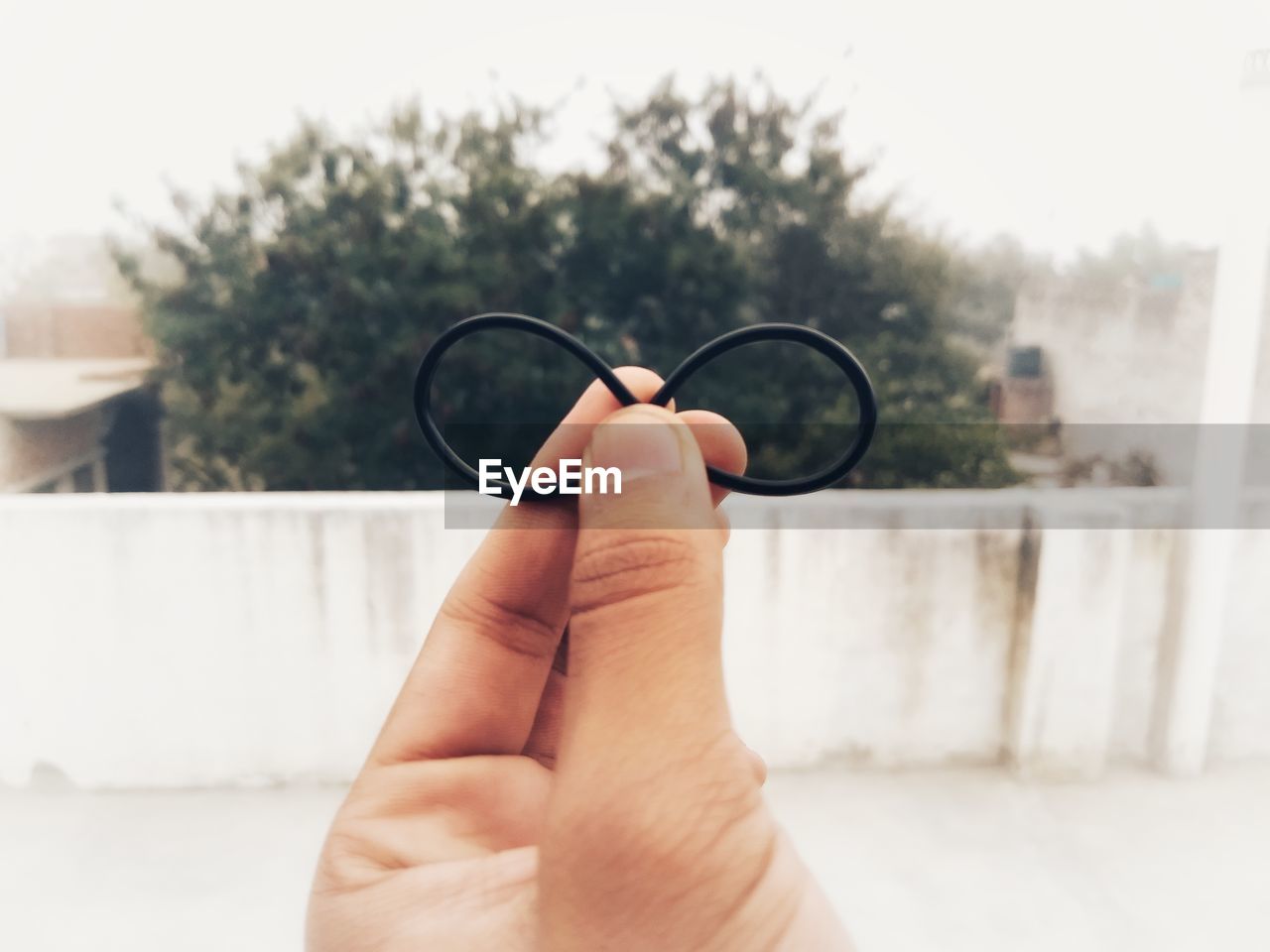 Cropped image of person holding rubber band against sky