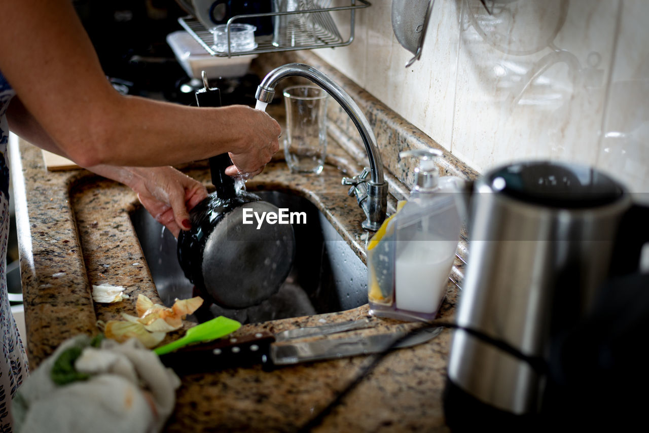 Hands of a woman washing pan in the kitchen sink.