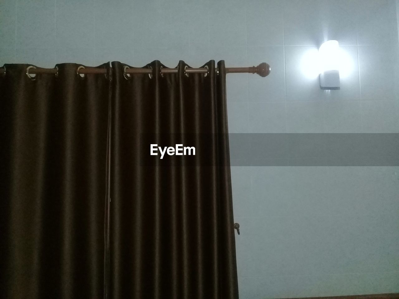LOW ANGLE VIEW OF ILLUMINATED LAMP ON WALL AT HOME