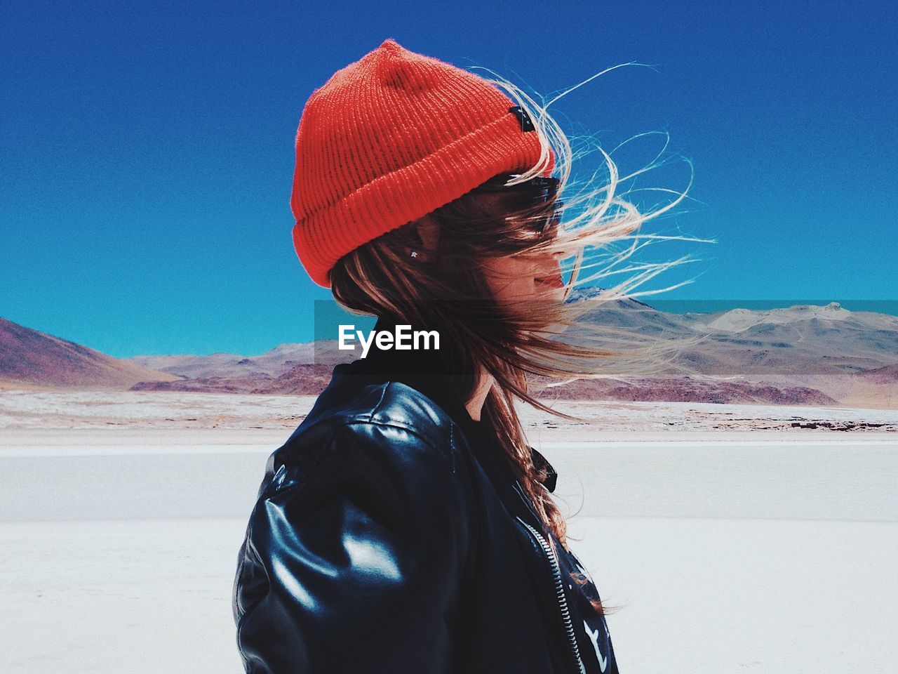 Side view of woman with tousled hair standing in desert against blue sky