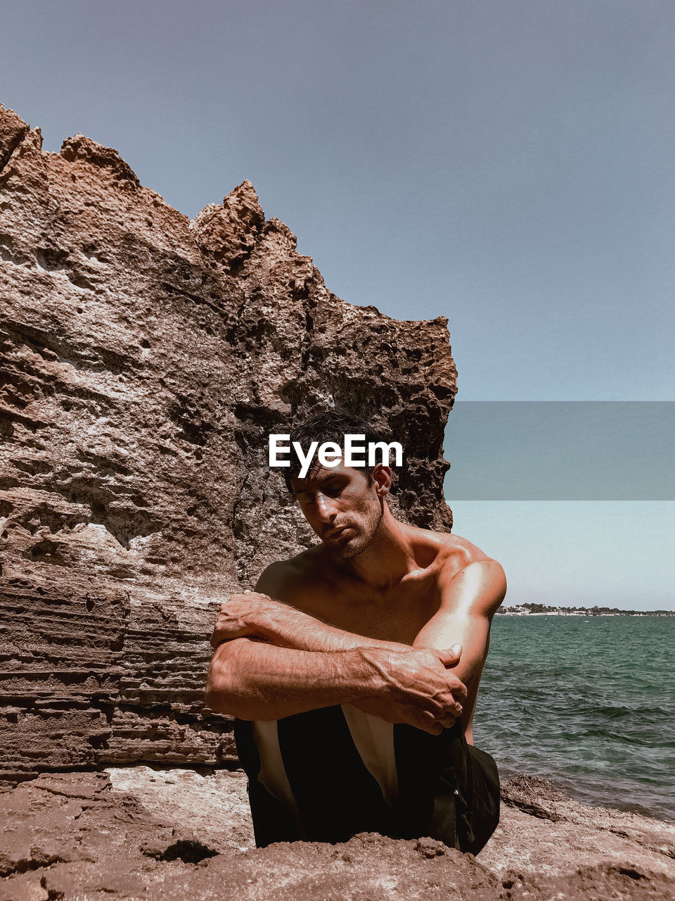 YOUNG MAN ON ROCK AGAINST SEA