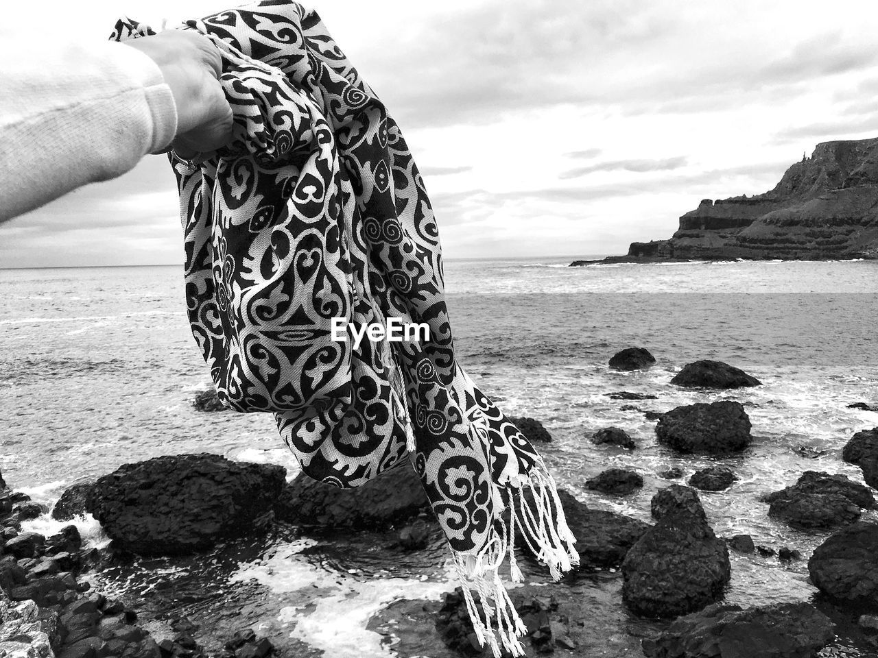 Cropped hand holding scarf at beach against sky