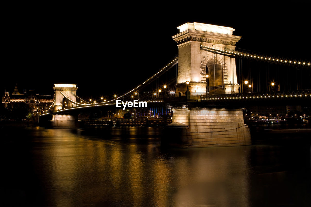 ILLUMINATED BRIDGE OVER RIVER WITH CITY IN BACKGROUND