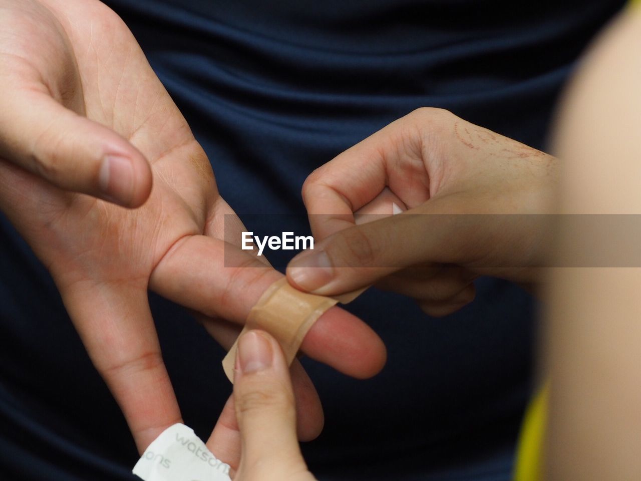 Cropped hand of woman putting adhesive bandage on finger of person