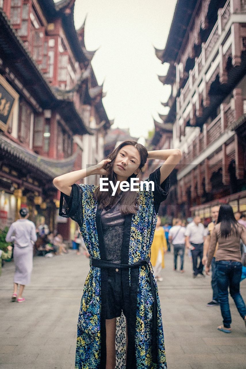 PORTRAIT OF SMILING YOUNG WOMAN STANDING ON STREET