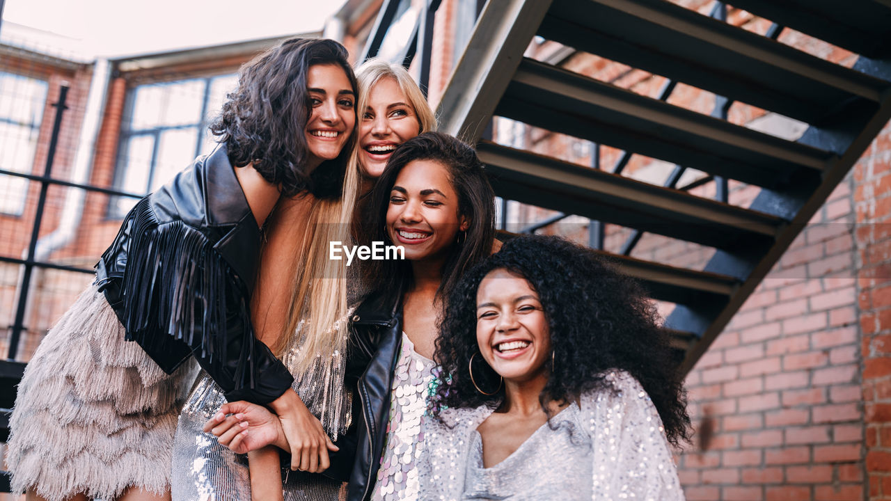 Low angle view of cheerful young female friends standing on staircase against building