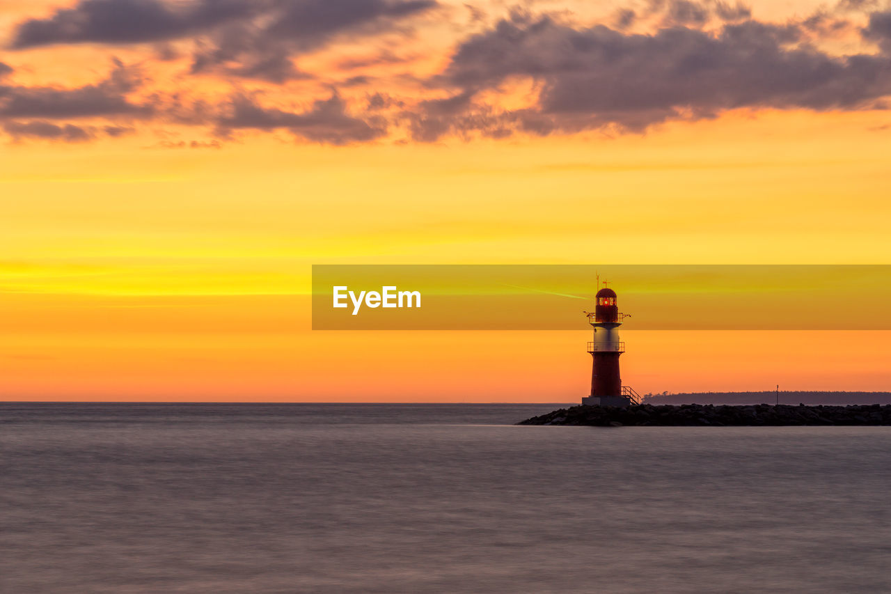 Lighthouse by sea against orange sky