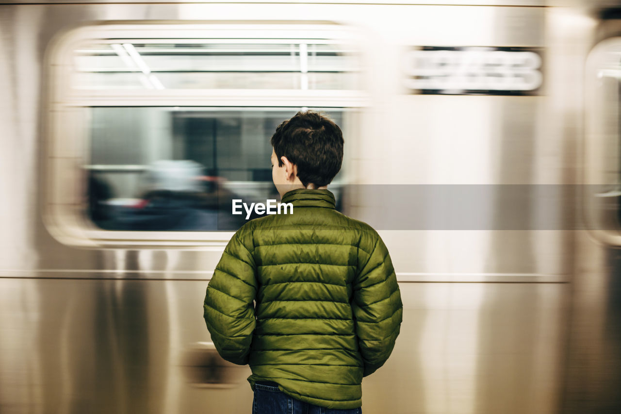 Rear view of boy wearing green jacket while standing at subway station