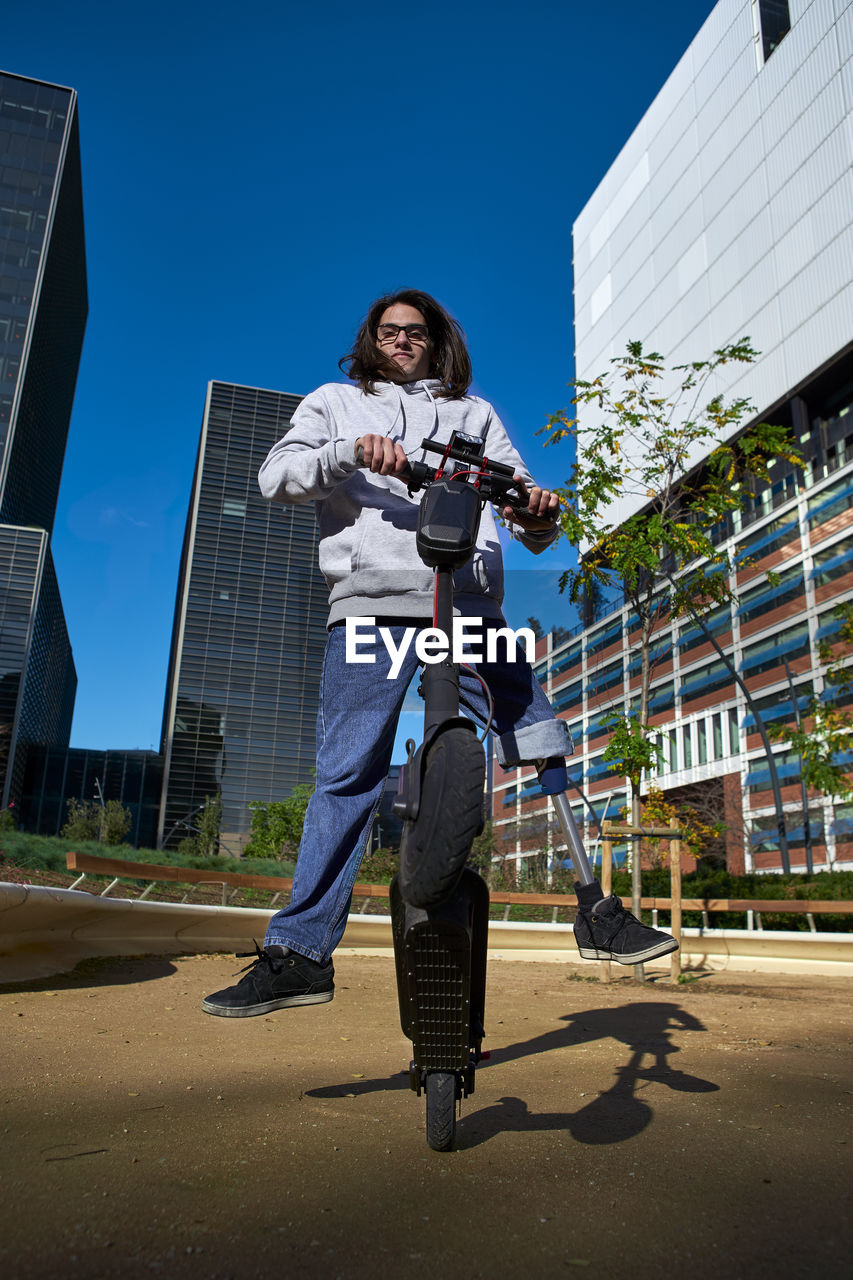 Young disabled man practicing stunt on electric push scooter in playground against buildings in city