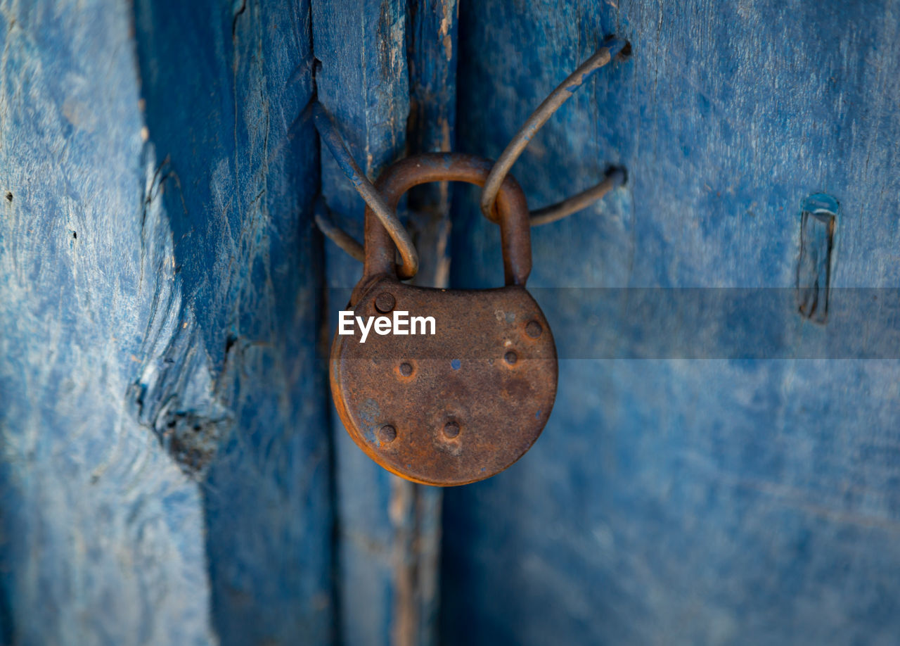 Close-up of rusty padlock hanging on wooden door