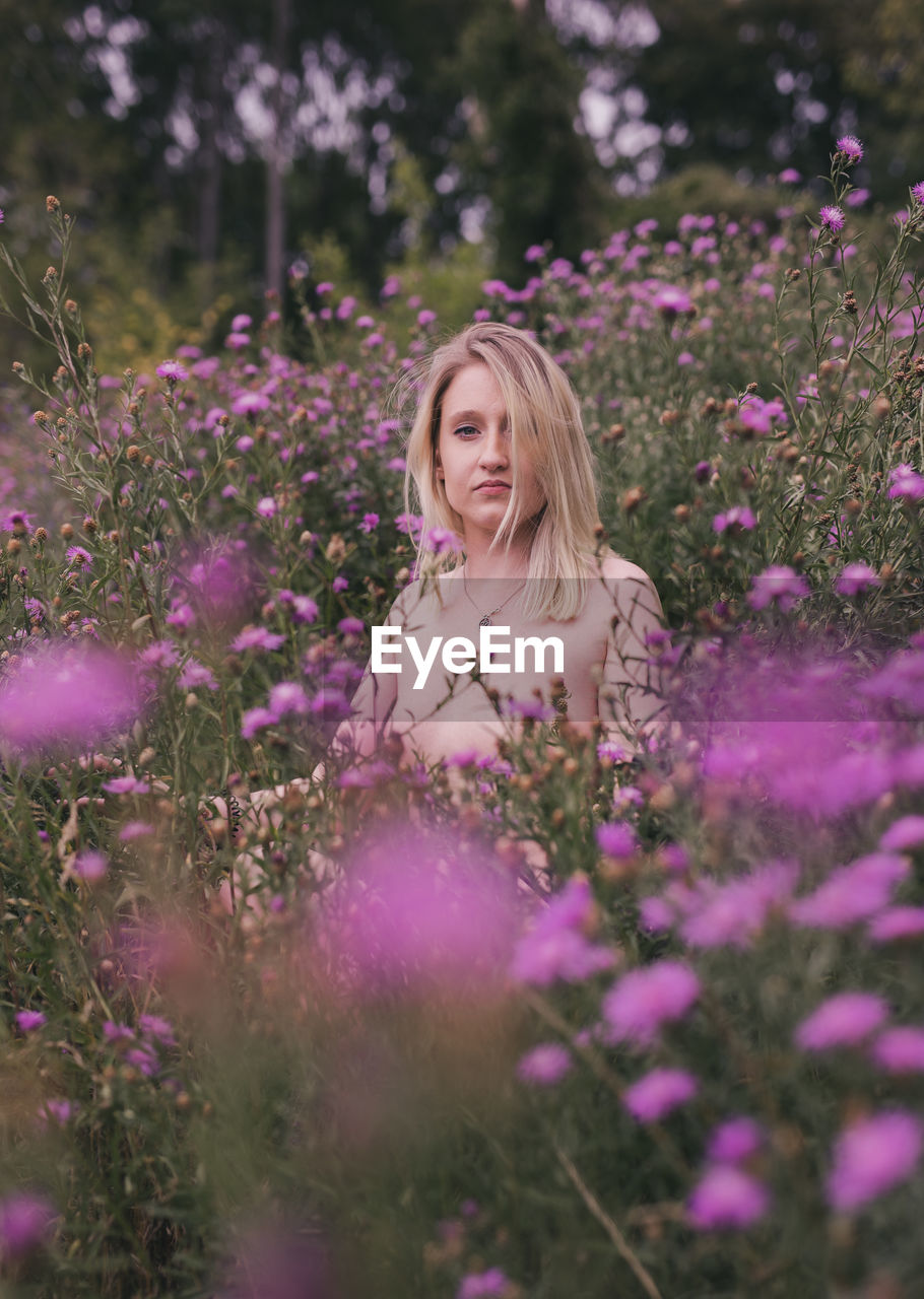 Beautiful young woman standing by purple flowering plants on field