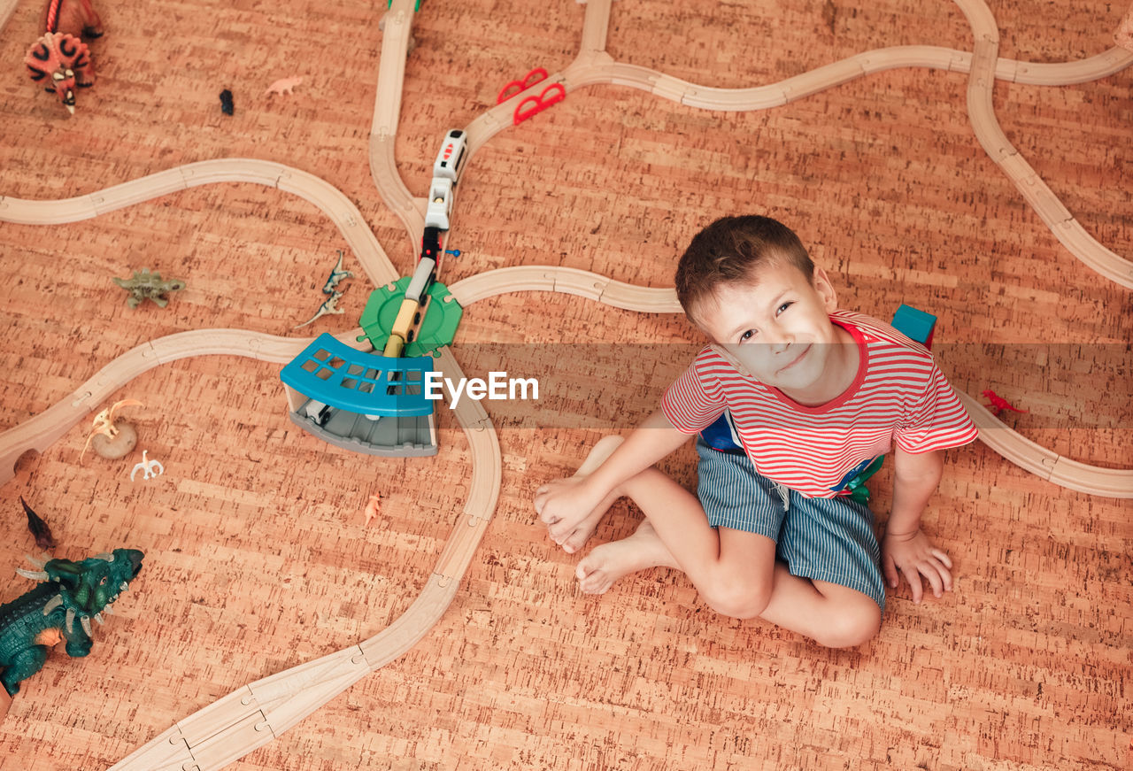 Child plays with wooden railway road in his room, top view