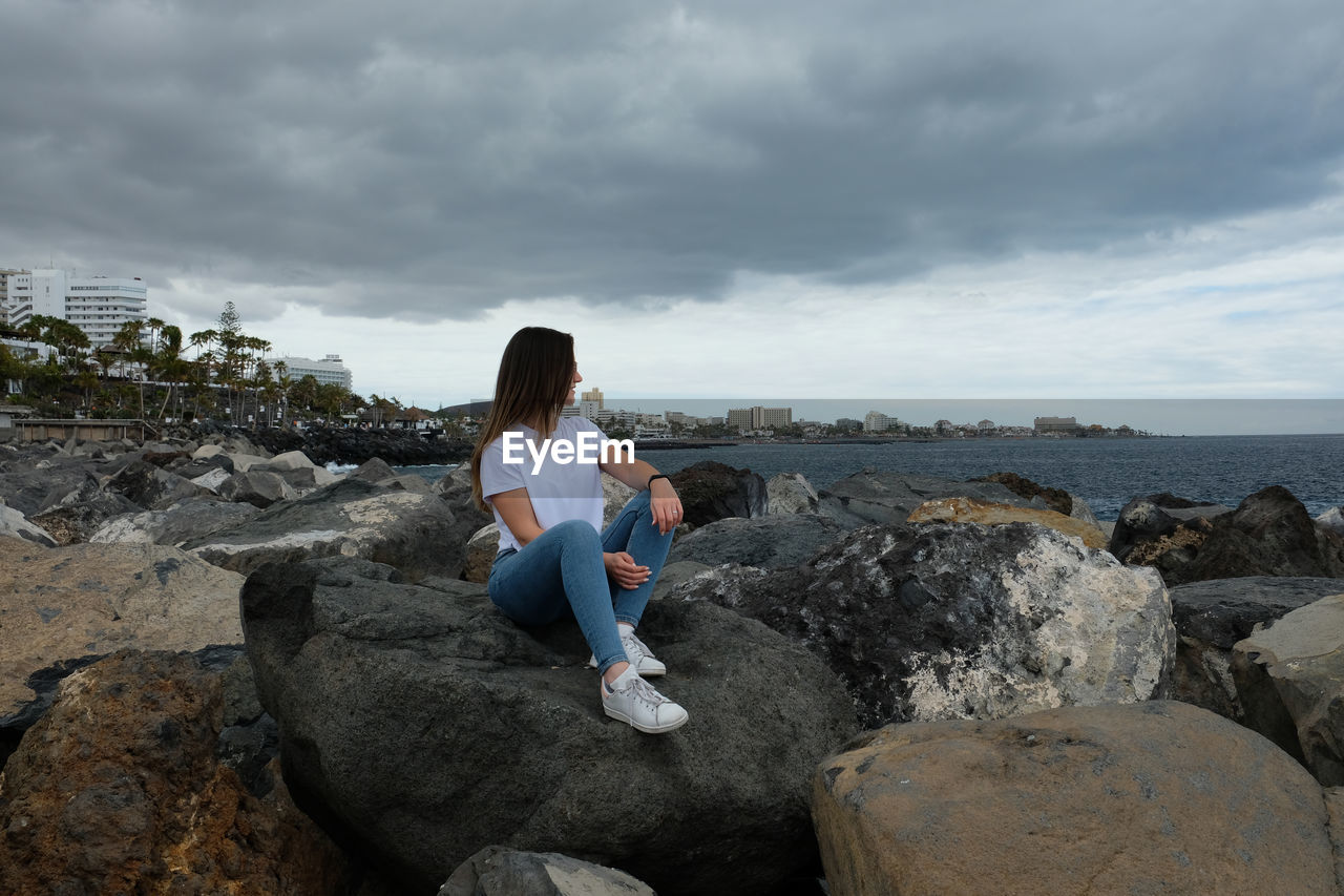 Woman sitting on rock by sea against sky