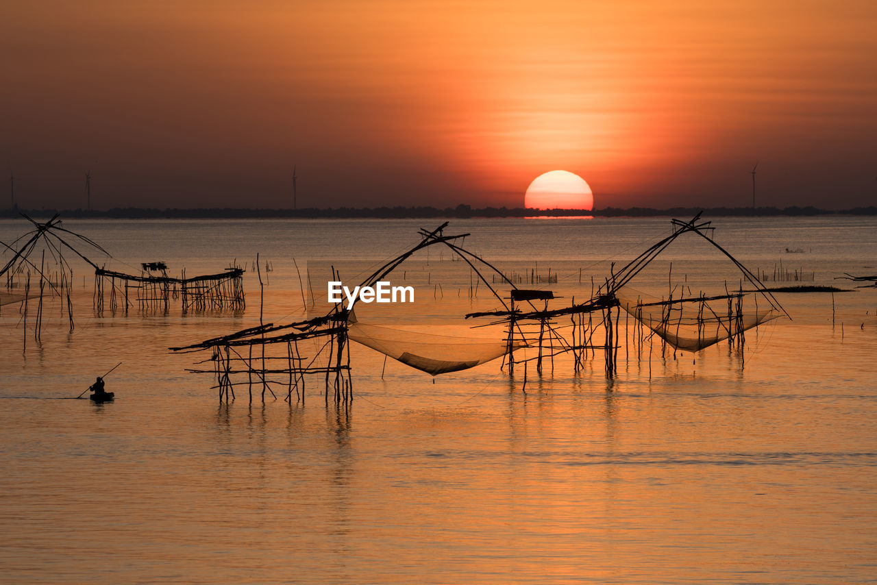 Silhouette fishing nets in sea against orange sky