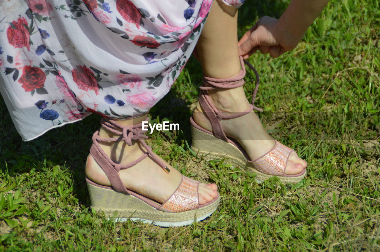 Low section of woman tying sandal lace on grassy field