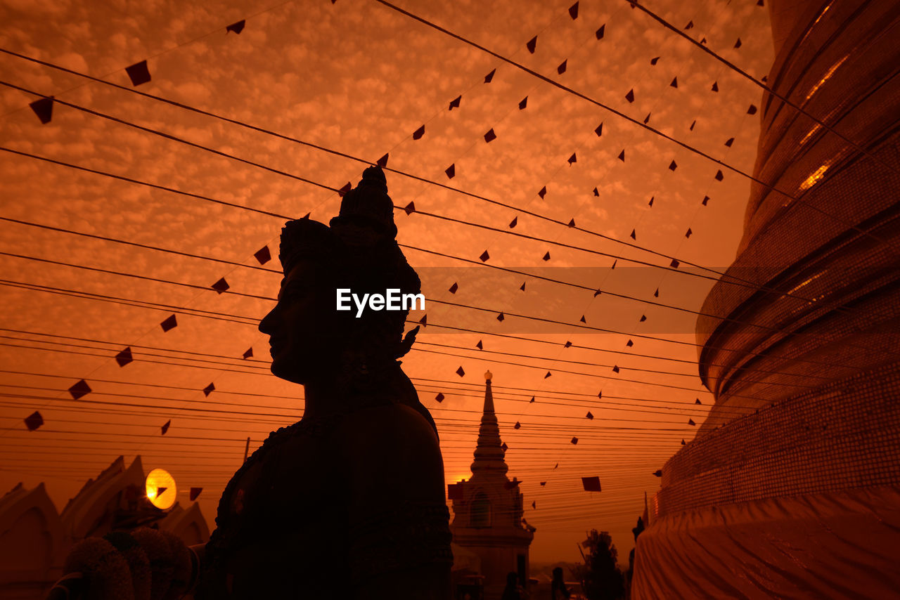 Low angle view of decorations and stature at temple against orange sky during sunset