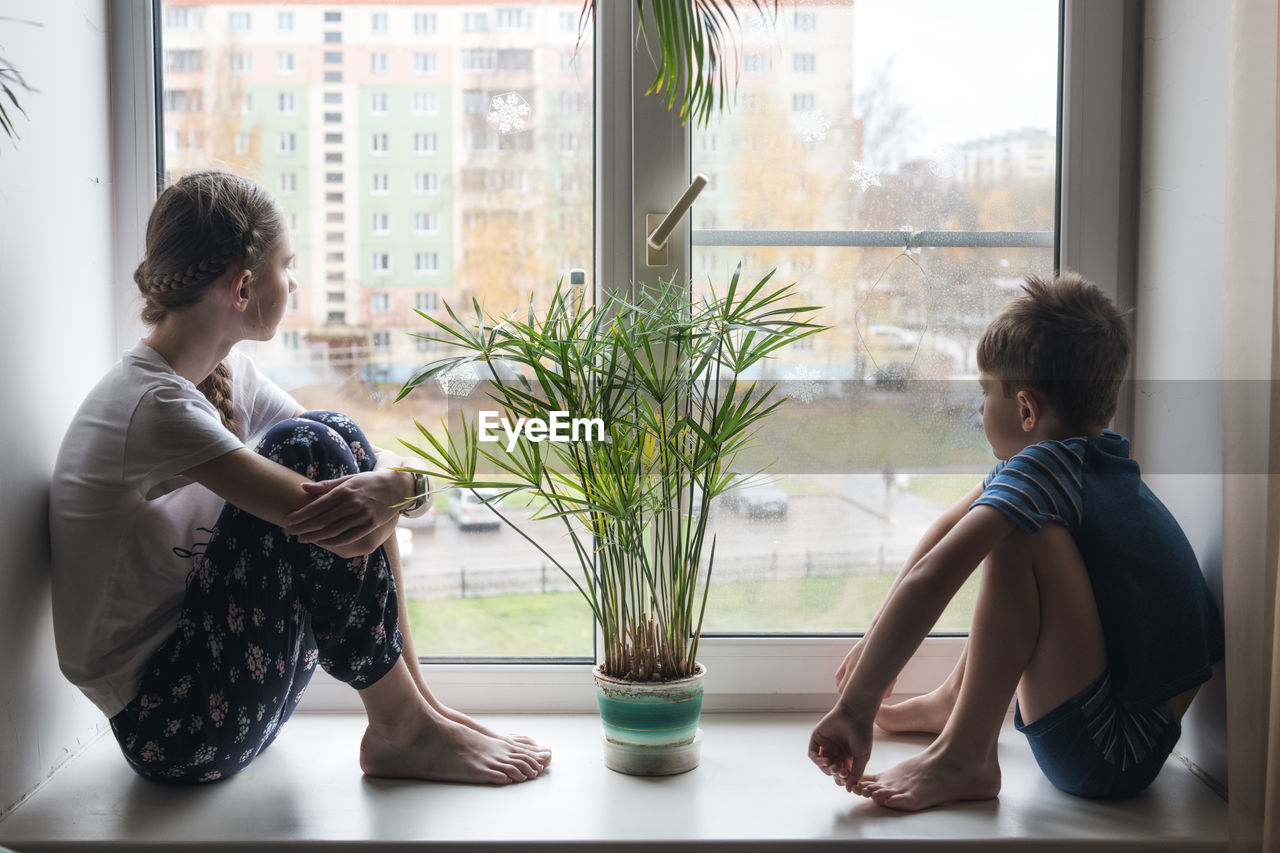 Side view of children sitting against window